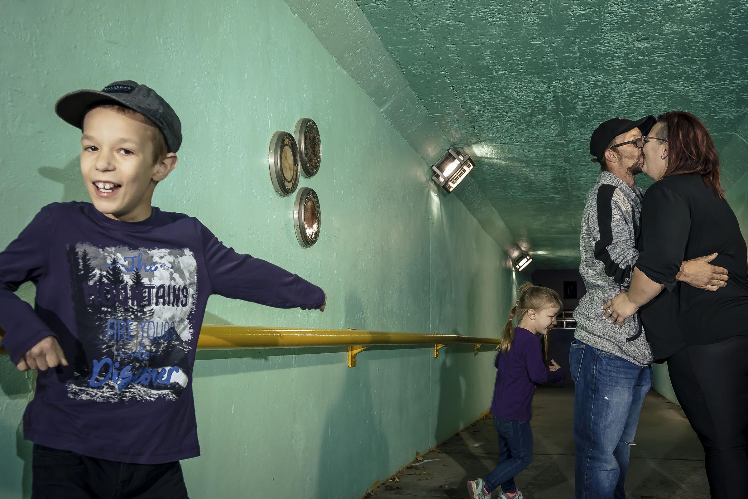 Portrait famille jeune garçcon pointe ses parents qui s'embrasse dans un tunnel milieu urbain par Tobi Malette photographe Vaudreuil-Soulanges et ouest de l'ile de montreal
